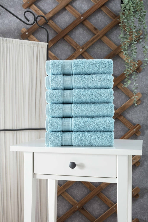 Krombee presents Stack of light blue towels on a white table with a wooden lattice and plant in the background