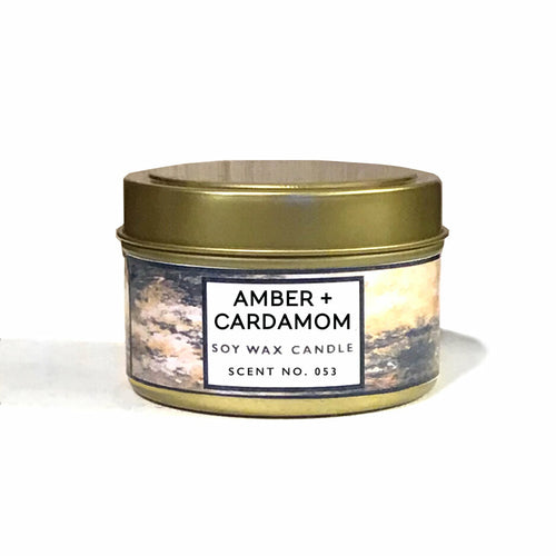 Soy wax candle in a tin with 'Amber + Cardamom' label on a white background
