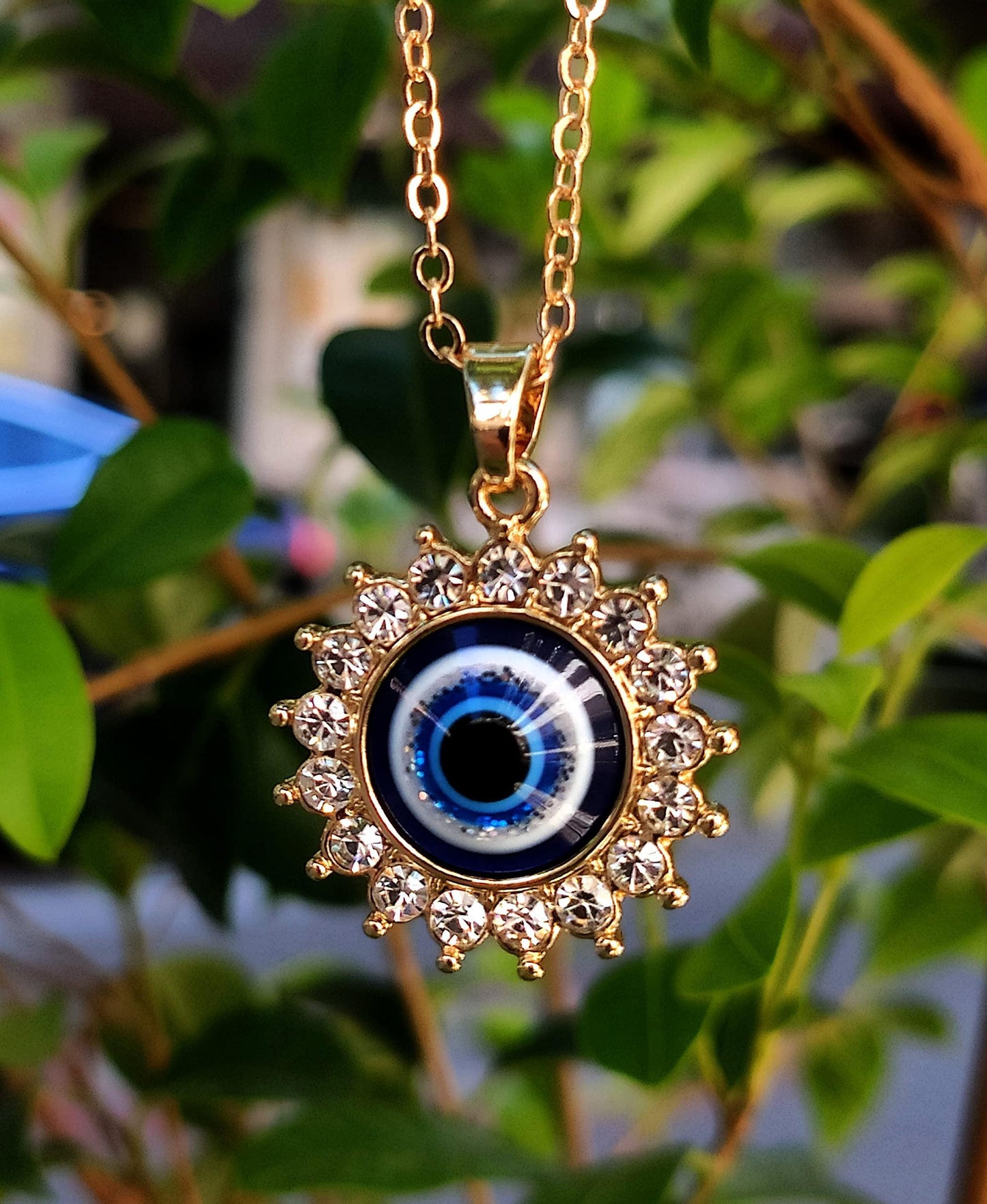 Gold evil eye charm necklace with under sun and natural background detail