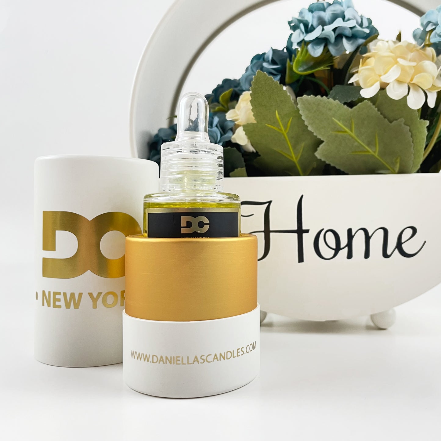 White and gold candle with 'DC' branding next to a mug and decorative plant on a white background