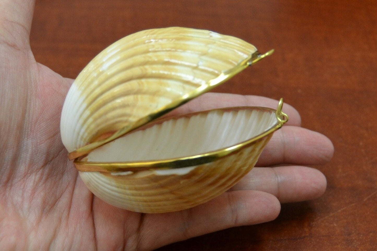 Shell-shaped trinket box with gold interior held in a hand on a wooden surface
