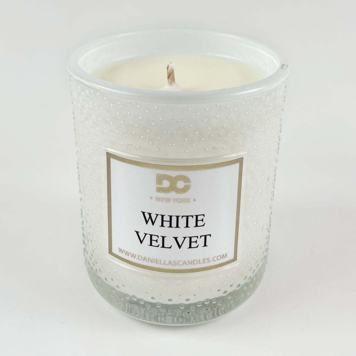 White candle in a textured glass jar with a label on a white background