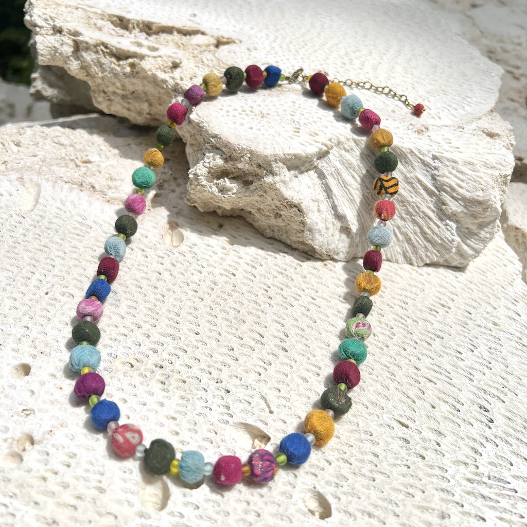 Colorful handcrafted Kantha Bead Necklace displayed on beach sand and rock – eco-friendly recycled sari jewelry handmade in India