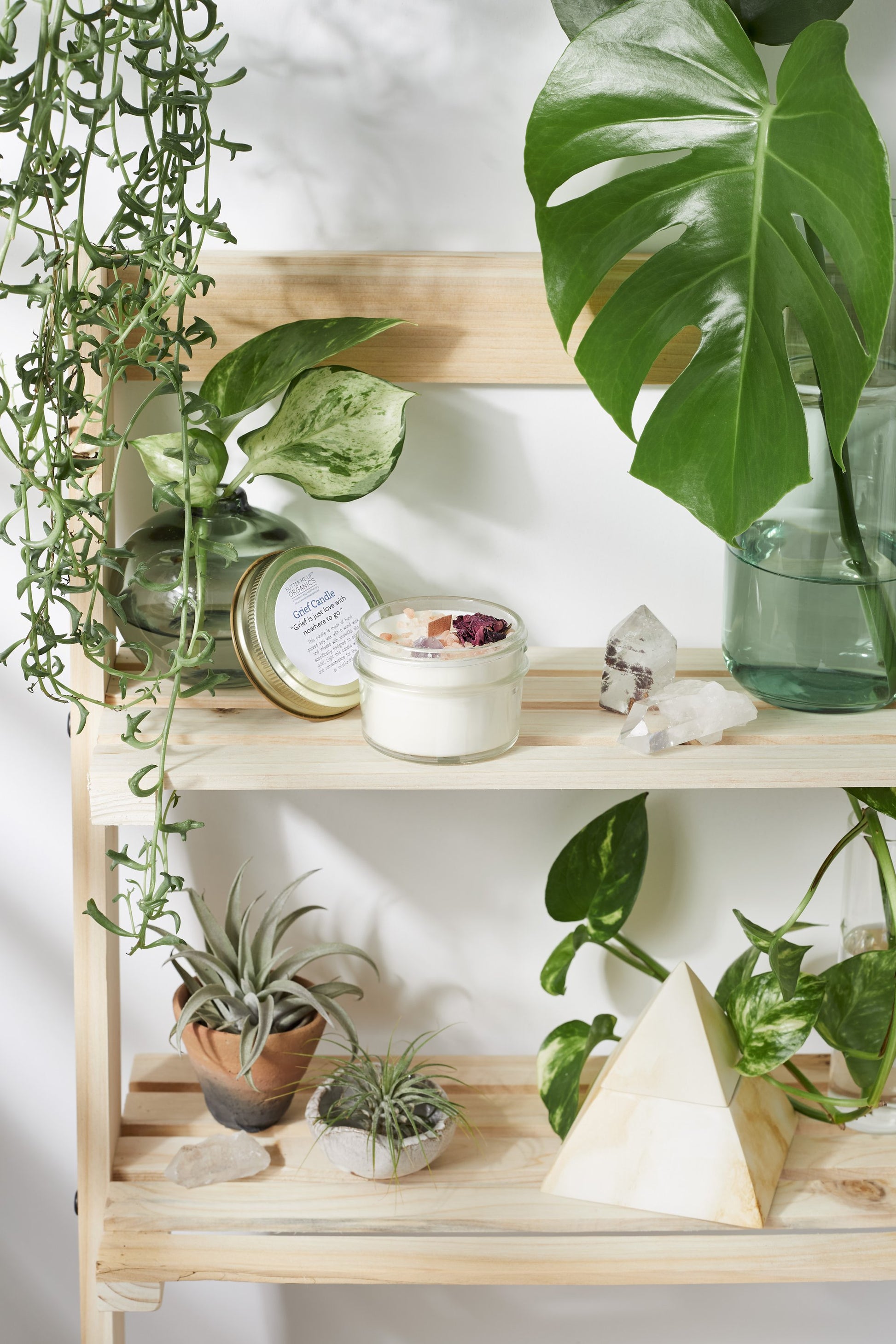 Wooden shelf with plants, Krombee Remembrance Candle, and decorative items against a white wall.