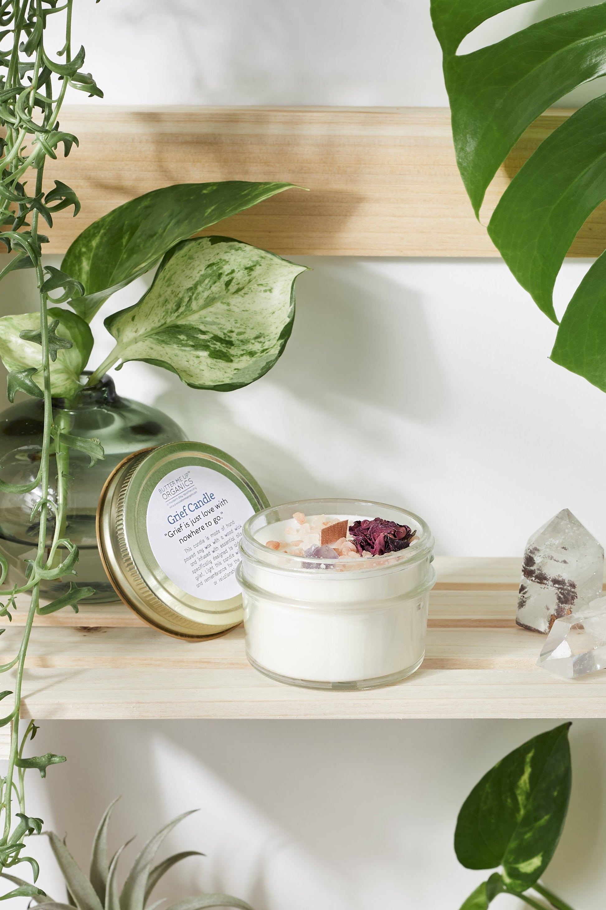 Krombee Remembrance Candle in a glass jar on a wooden shelf with plants around