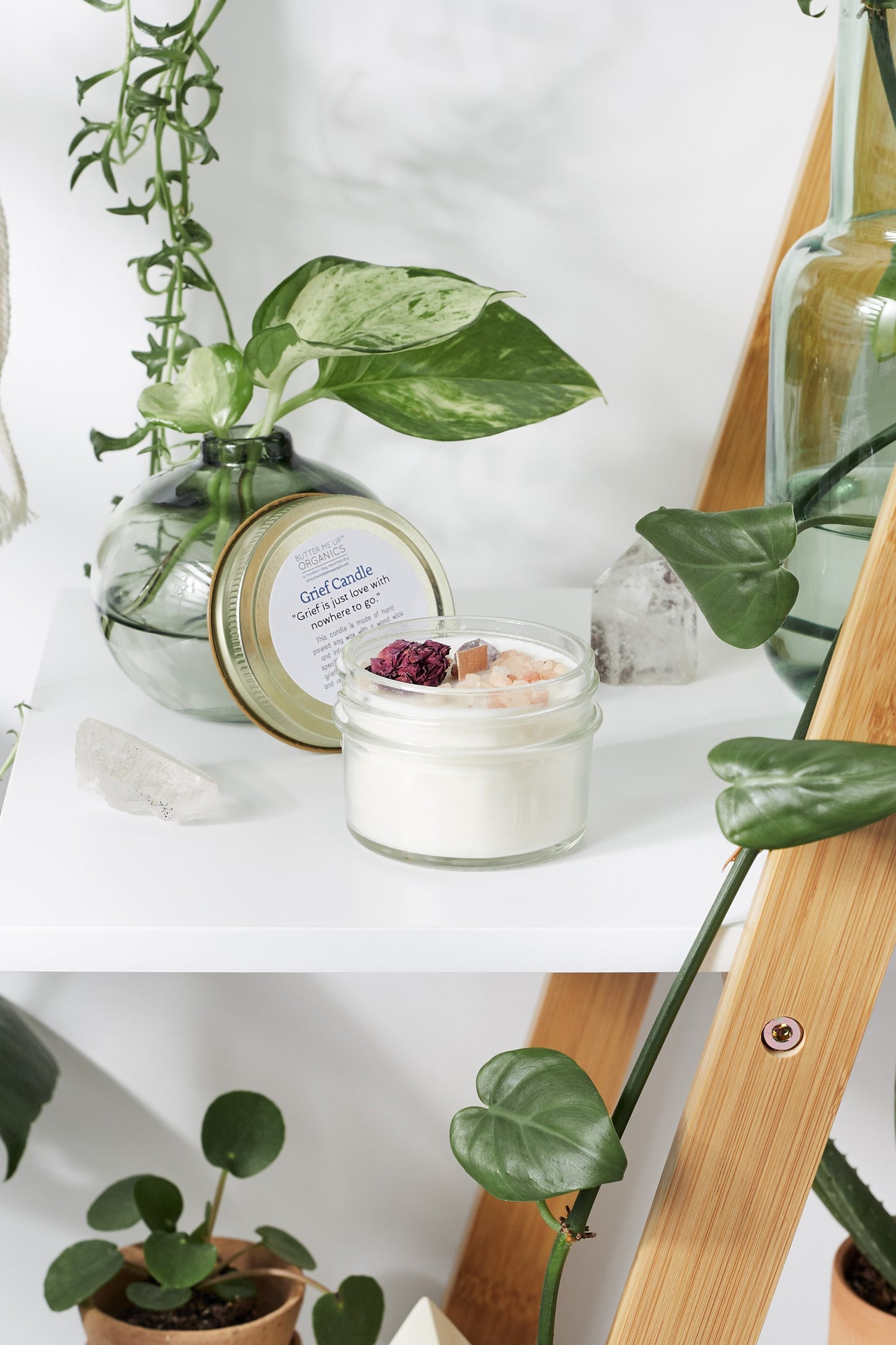 Small jar of Krombee Remembrance Candle on a white surface with plants and decorative items.
