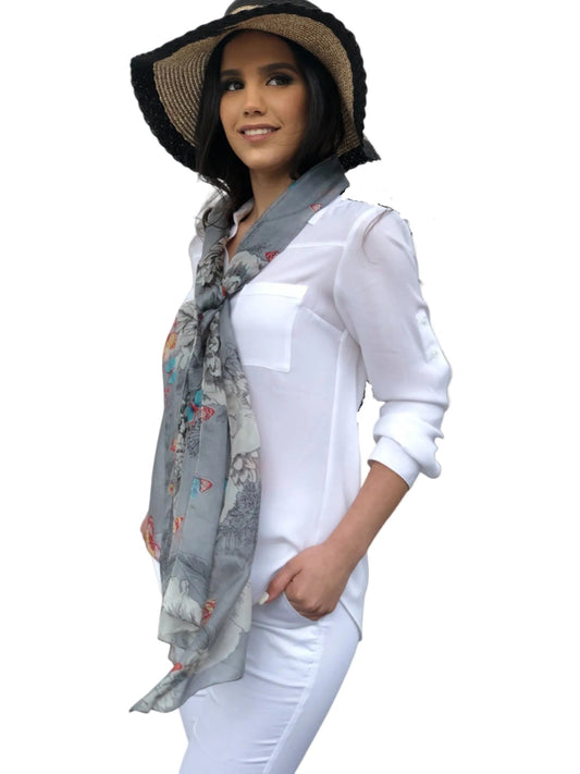 Woman wearing a white outfit with a floral scarf and wide-brimmed hat against a light background