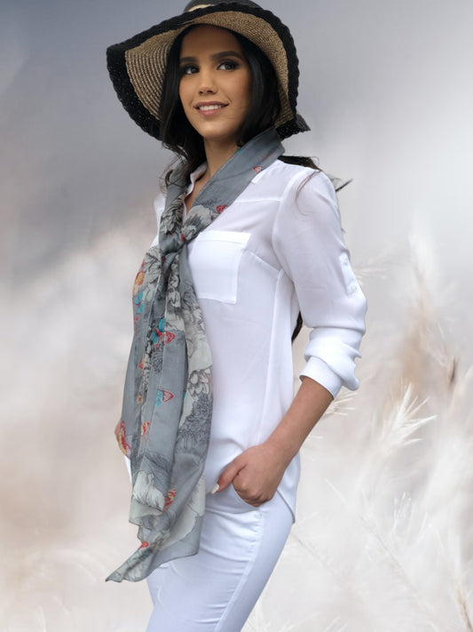 Woman wearing a white outfit with a floral scarf and wide-brimmed hat against a light background