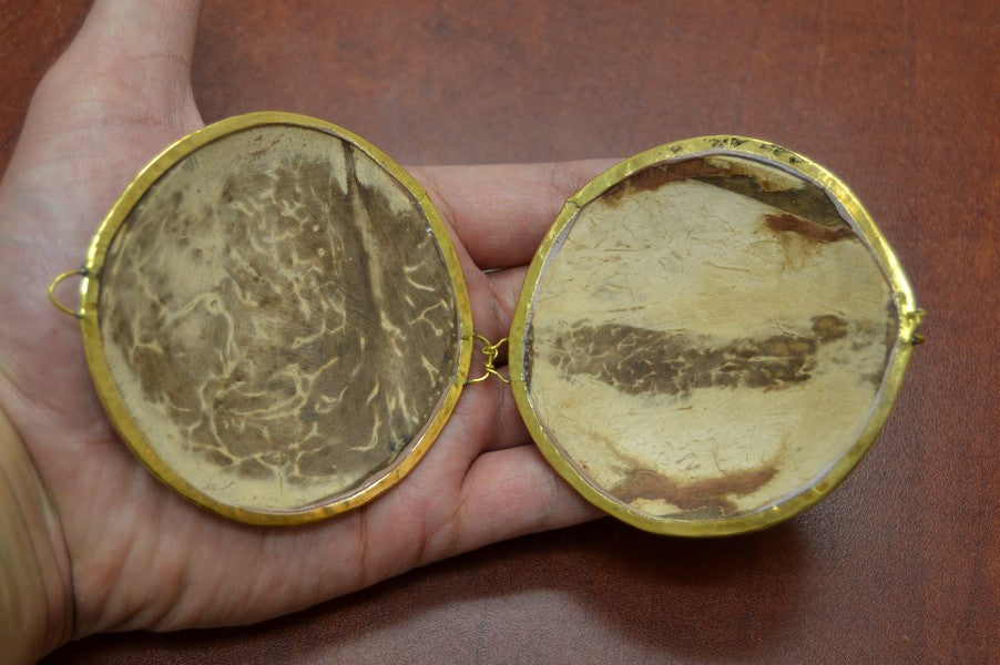 Two round, gold-framed mirrors held in a hand against a brown background
