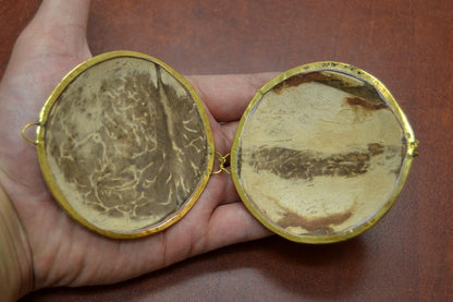 Two round, gold-framed mirrors held in a hand against a brown background
