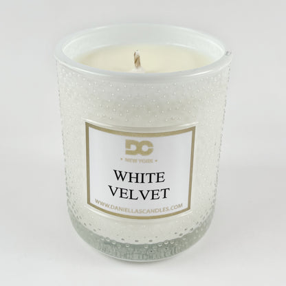 White candle in a textured glass jar with a label on a white background