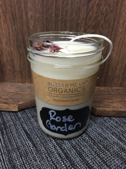 Butter Me Up Organics candle labeled 'Rose Garden' on a textured surface with wooden background