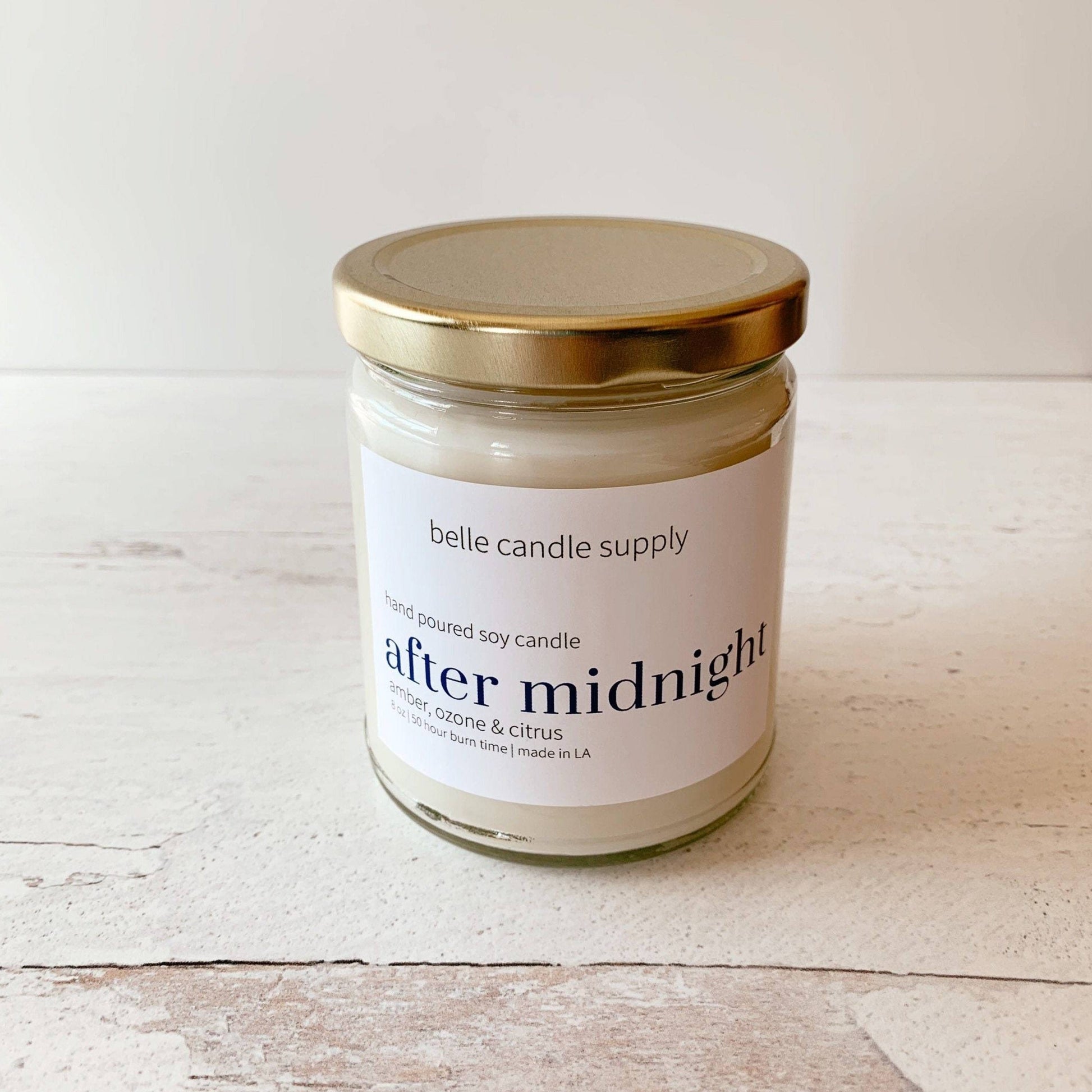 Jar candle labeled 'after midnight' by belle candle supply on a wooden surface.