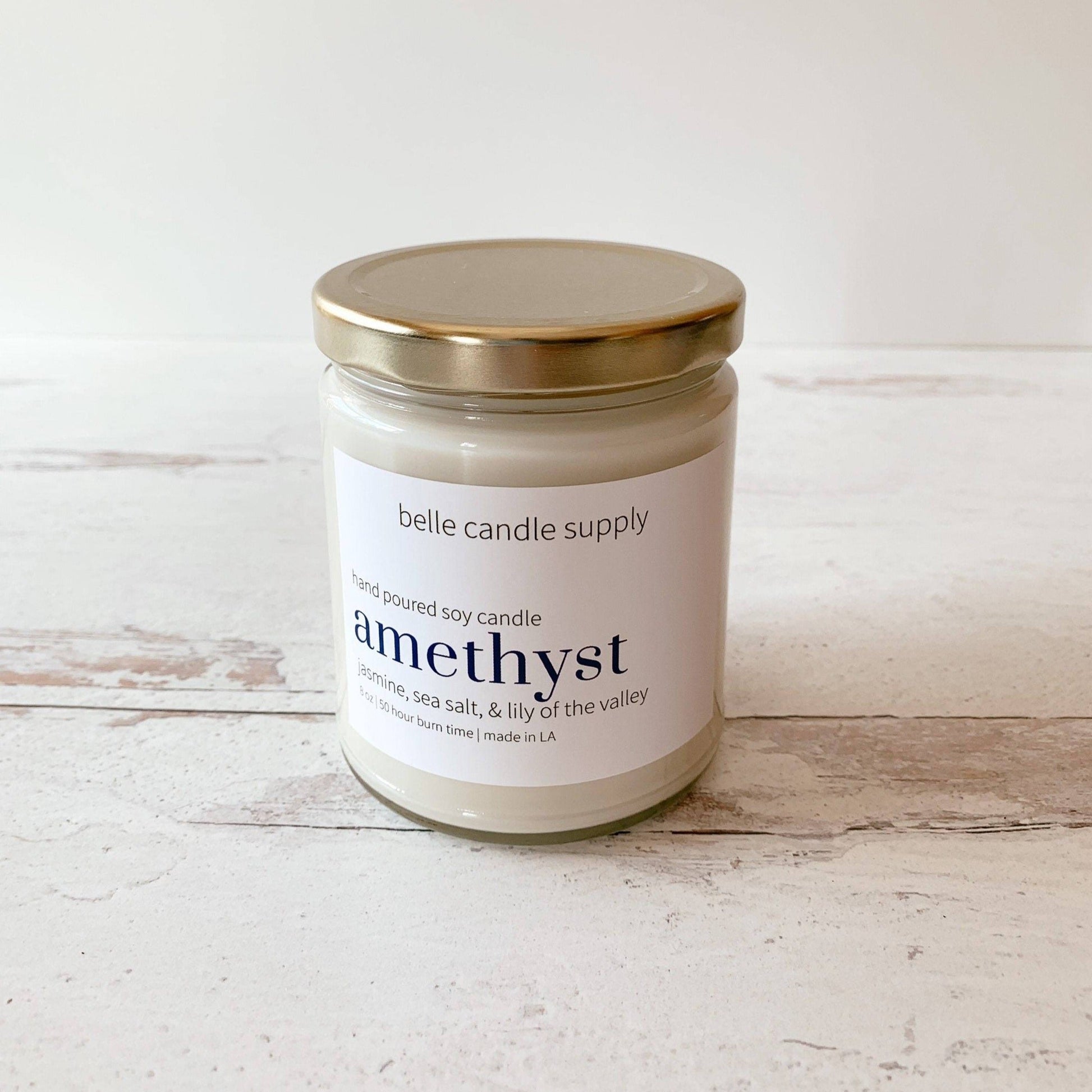Candle jar labeled 'amethyst' from belle candle supply on a wooden surface