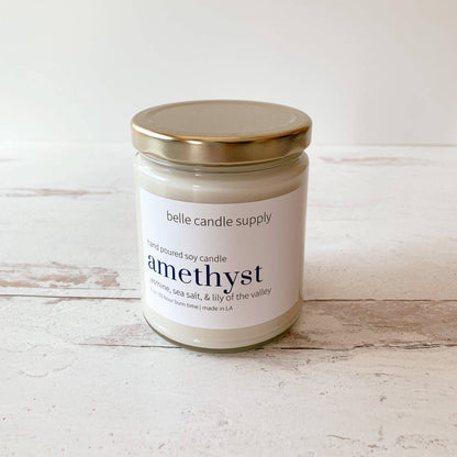 Candle jar labeled 'amethyst' from belle candle supply on a wooden surface