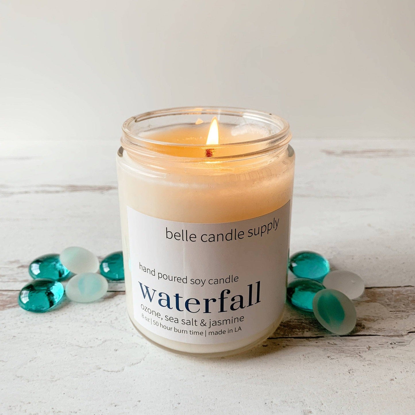 Candle with 'belle candle supply' label on a wooden surface with decorative stones.