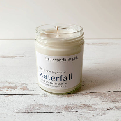 Candle in a glass jar labeled 'belle candle supply' on a wooden surface