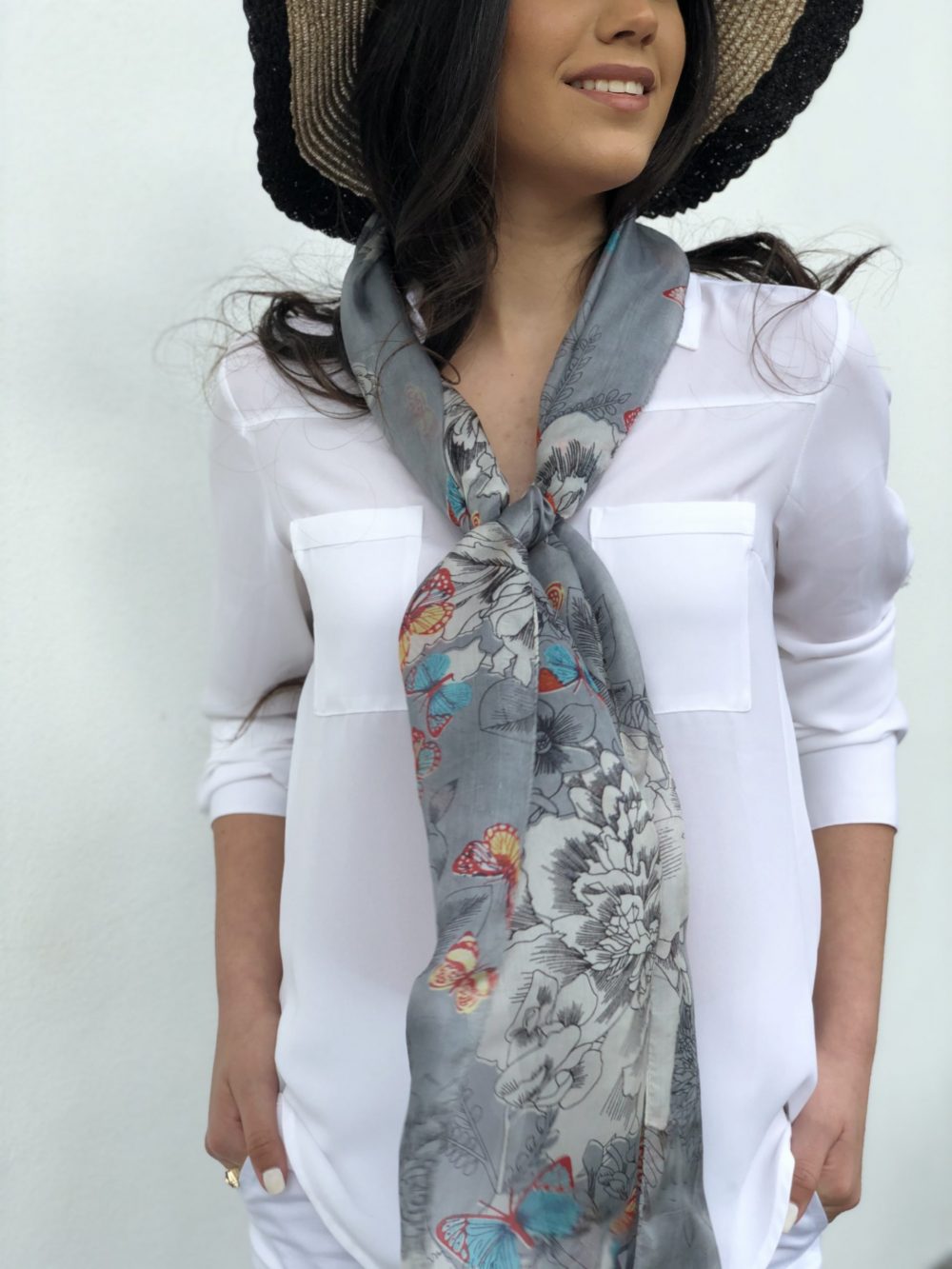 Woman wearing a white shirt with a floral scarf and a wide-brimmed hat against a plain background