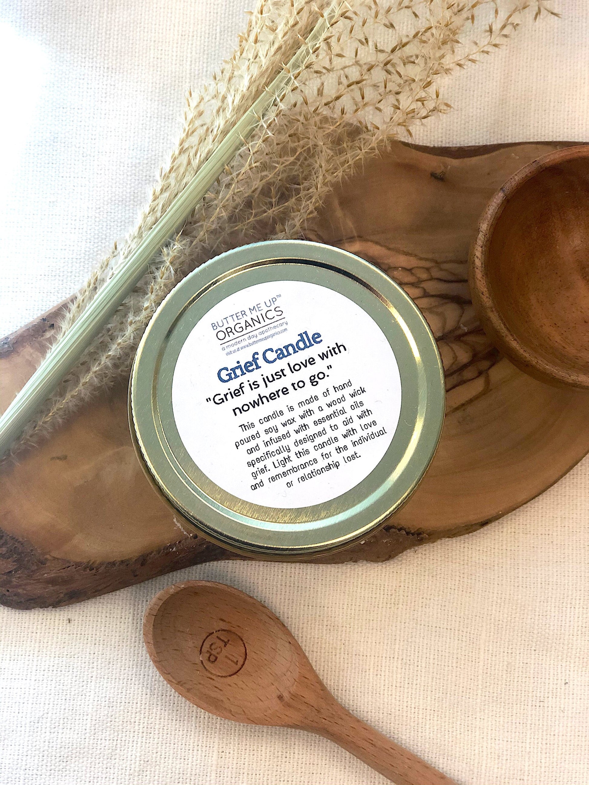 Krombee Remembrance Candle jar with lid featuring text on a wooden surface with a spoon and dried plants.