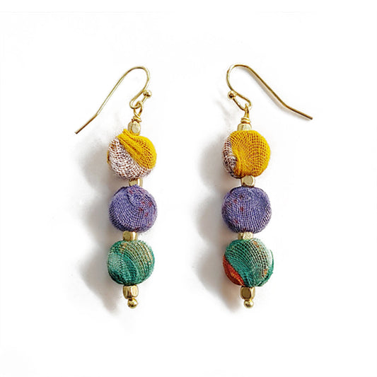 Close-up of vibrant Kantha Sari Earrings made from colorful recycled sari fabric and brass beads.